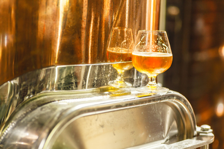 Glass with amber ale beer standing on a metal doorway of a copper lauter tun at a breweryの写真素材