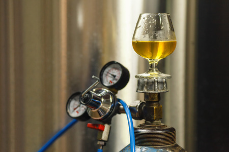 Tasting glass with clear lager beer standing on a gas tank at a breweryの写真素材