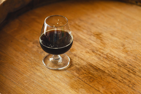 Glass of black stout beer standing on a wooden barrel in a breweryの写真素材