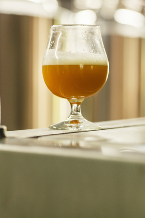 Glass full of wheat beer standing on brewing equipment at a breweryの写真素材