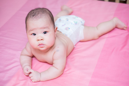 Asian baby girl scowl on pink bed and she looking at the cameraの写真素材