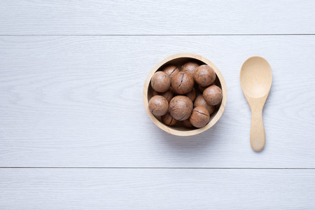 Macadamia in wooden bowl near wooden spoon on white wooden tableの写真素材