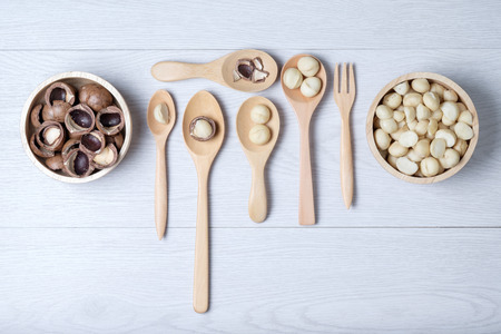 Macadamia nuts and shell in wooden bowl and spoons put on white wooden tableの写真素材