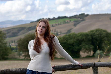 Sad girl with green eyes stands near fence with beautiful landscape background. Tuscan, Italyの写真素材