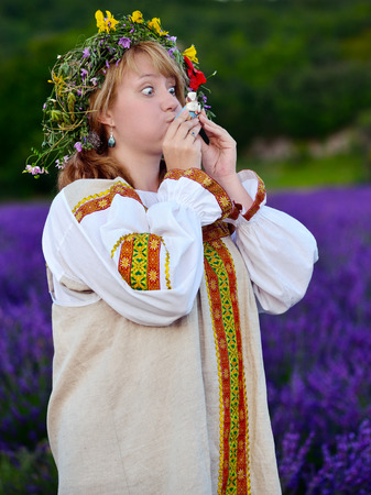 Funny peasant girl with eyes wide in russian national dress blows the whistle toyの写真素材