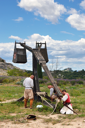 LES BAUX, FRANCE - JUL 9, 2014: Amateur historical reconstruction of medieval wars. Mens dressed as medieval warrior charge the catapult for fire. Les Baux castleのeditorial素材