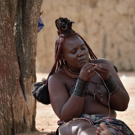 KAMANJAB, NAMIBIA - FEB 1, 2016: Unidentified working Himba woman with the typical necklace and hairstyle shown in himba tribe villageのeditorial素材