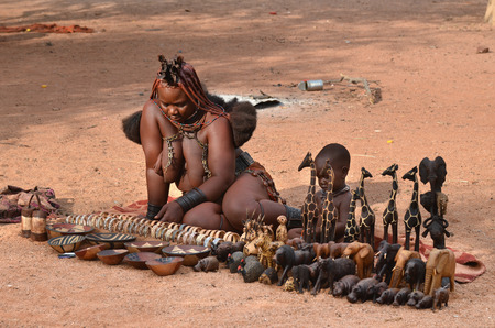 KAMANJAB, NAMIBIA - FEB 1, 2016: Unidentified Himba woman with the typical necklace and hairstyle sales the primitive souvenirs in village marketのeditorial素材