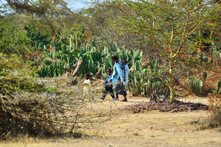 Kenya, Africa - Aug 22, 2010: African woman with children going through a bush carrying baby on her back. Tanzania. Africaのeditorial素材