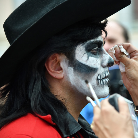 Moscow, Russia - June 29, 2018: The girl participant makes the sugar skull makeup on face a man during Dia de los Muertos Mexican carnival. Day of The Deadのeditorial素材