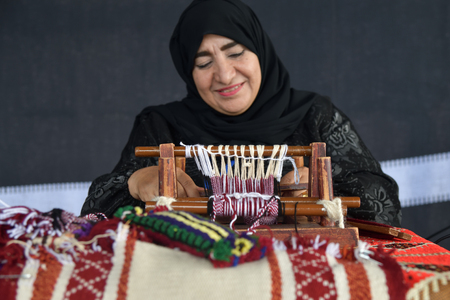 Moscow, Russia - July 14, 2018: A senior arabian woman makes a traditional sadu weaving. Focus on the frame. Qatarのeditorial素材