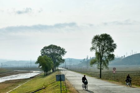 North Korea, Pyongyang - April 30, 2019: Countryside landscape, DPRK. Men ride a bikes on a rural road at sunriseのeditorial素材