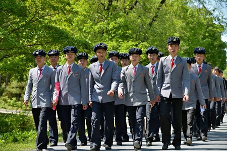 North Korea, Pyongyang - May 1, 2019: A group of North Korean workers in identical suits marching along the road. DPRKのeditorial素材