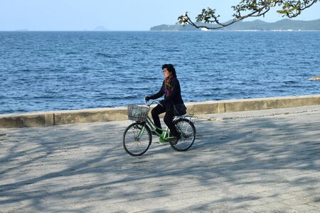 Wonsan, North Korea - May 3, 2019: Local woman on a bike rides along the sea on the promenade of the Japanese or Eastern Sea in Wonsanのeditorial素材
