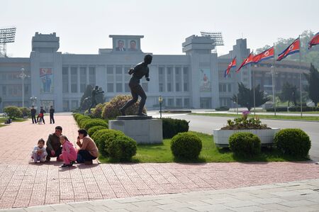 Pyongyang, North Korea - May 1, 2019: A family of locals sits on the sidewalk in front of the Kim Il Sung Stadiumのeditorial素材