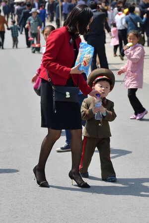 Pyongyang, North Korea - May 1, 2019: Young mom and socks, dressed as little women, are walking on Pyongyang street. Baby keeps a bottle of waterのeditorial素材