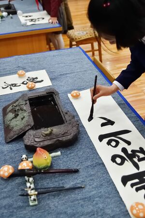 North Korea, Pyongyang - May 2, 2019: Girl writing black hieroglyphs on a white sheet of paper. Pyongyang Palace of schoolchildren. Extracurricular educational institutionのeditorial素材