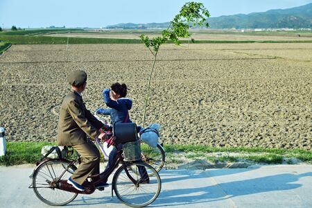 Wonsan region, North Korea - May 3, 2019: A local people riding a bikes along the country road. Ð¡ountryside, nearby Wonsan port. Man and womanのeditorial素材