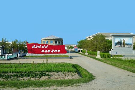 Wonsan region, North Korea - May 3, 2019: Typical houses of peasants built by the state for residents of countryside. DPRK. Village, propaganda banner and agricultural fieldのeditorial素材