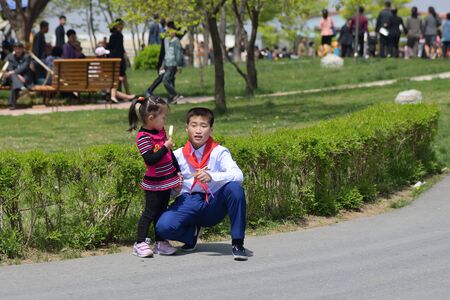 Pyongyang, North Korea - May 1, 2019: Young boy, member of the Young Pioneer Corps and his little sister with ice cream on a city streetのeditorial素材