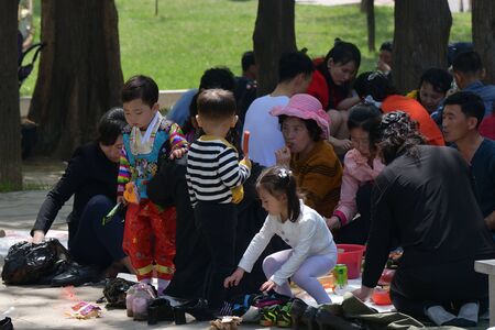 Pyongyang, North Korea - May 1, 2019: Happy families having fun outdoor at bbq picnic with snacks, food and drink. Local people enjoying spring time together at barbecue park partyのeditorial素材