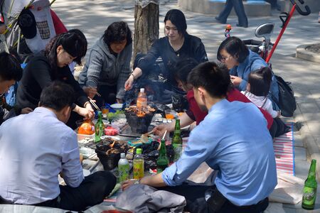 Pyongyang, North Korea - May 1, 2019: Happy family having fun outdoor at bbq picnic with snacks, food and drink. Local people enjoying spring time together at barbecue park partyのeditorial素材