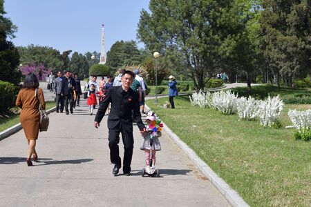 Pyongyang, North Korea - May 1, 2019: little girl on scooter holds the hand of her father on the Pyongyang streetのeditorial素材