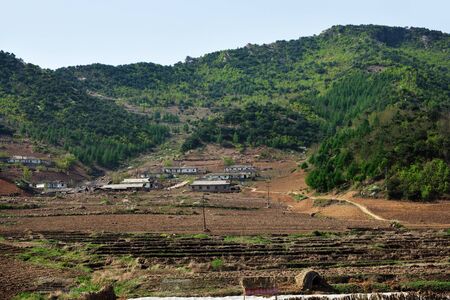 Wonsan region, North Korea - May 3, 2019: Typical houses of peasants built by the state for residents of countryside. Hillside village and agriculture fields, mountains in the backgroundのeditorial素材