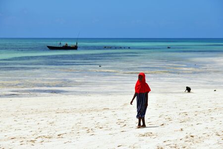 Kendwa, Zanzibar - October 4, 2019: Little local girl in traditional red hijab on beach. Tanzania, Africaのeditorial素材