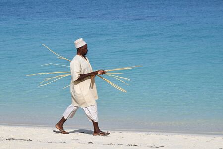 Kendwa, Zanzibar - October 6, 2019: Local man in traditional dress goes along a ocean on Kendwa...