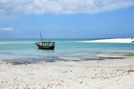 Zanzibar, Tanzania - October 4, 2019: Blue transparent water and wooden fishing boat on the Kendwa...