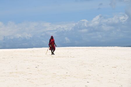 Kendwa, Zanzibar - October 4, 2019: Man from Masai tribe in traditional dress walks along Kendwa beach. Tanzania, Africaのeditorial素材