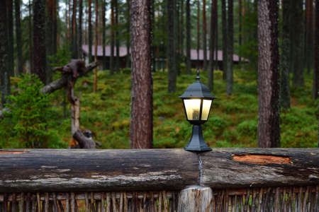 Lighted outdoor lamp on a wooden fence against the beautiful autumn pine forest. Russia, Karelia....