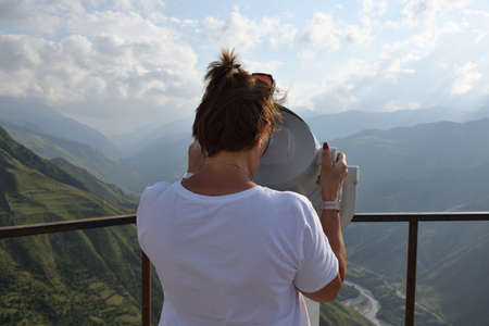 Woman watching in binocular on the valley between the Caucasus mountains. Observation point on a...