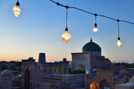 View to Mausoleum of Pahlavon Mahmoud.. Cityscape in Ichan Kala at sunset time, ancient inner town of the old city Khiva in Khorezm region, Uzbekistan. Focus on lampの写真素材