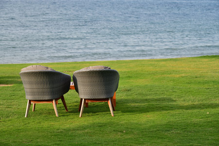 Two chairs on lawn before coastline. Al Bustan beach at early morning, most popular beach near city Muscat, Sultanate of Oman.の写真素材
