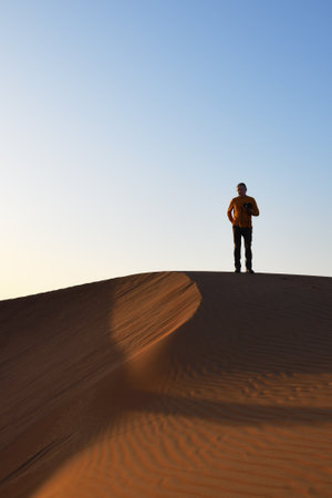 Tourist man with photo camera on top of dune in Rub Al Khali desert, Sultanate of Oman. Wahiba Sands dunes at sunset, Arabian Peninsulaの写真素材