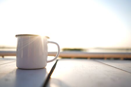 Stock Photo - Cup of tea on white wooden blurred sunset on river