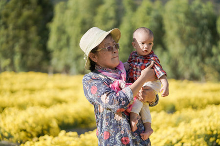 A cute baby boy with his grandmom spend time in a yellow flowers fields.の写真素材