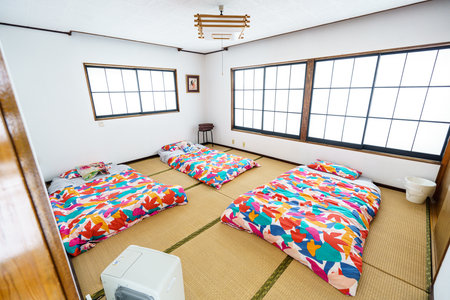 Bright and traditional Japanese-style room (Washitsu) with three vibrant futon bedding sets laid out on tatami mats, ready for guests. A comfortable and authentic sleeping experience for travelers or family.の写真素材