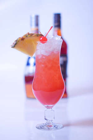 cocktail iced pineapple and cherries and bottles of alcohol in the backgroundの写真素材