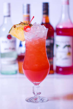 cocktail iced pineapple and cherries and bottles of alcohol in the backgroundの写真素材