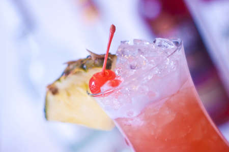 cocktail iced pineapple and cherries and bottles of alcohol in the backgroundの写真素材