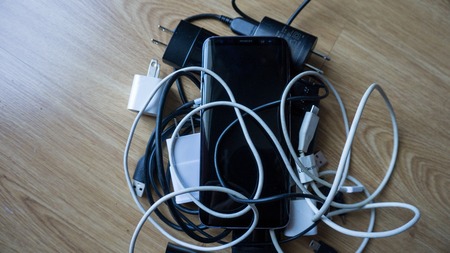 Smartphone tangled in differnt cables chargers usb and black and white wires