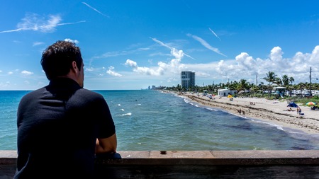 Young man looking at the view of Dania beach in Miami, Florida. USA. Summer sunny day with many people swimming in the waterの写真素材