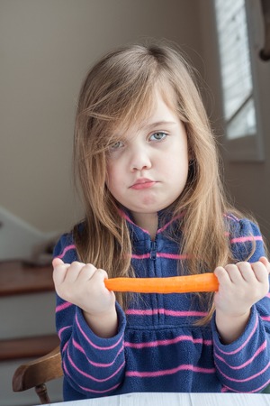 little unhappy girl playing with a carrotの写真素材