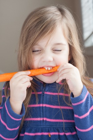 funny little girl biting a long carrotの写真素材