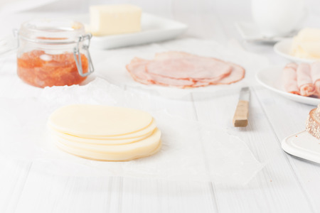 sliced of cheese served for breakfast with cold cuts, jam and bread at the backgroundの写真素材