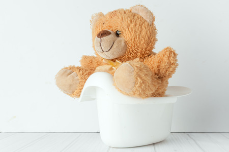 A teddy bear in a white potty next to stack of diapers. Conceptual image representing potty trainingの写真素材