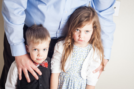 brother and sister held by their father, with guilt on their faces, great parenting image